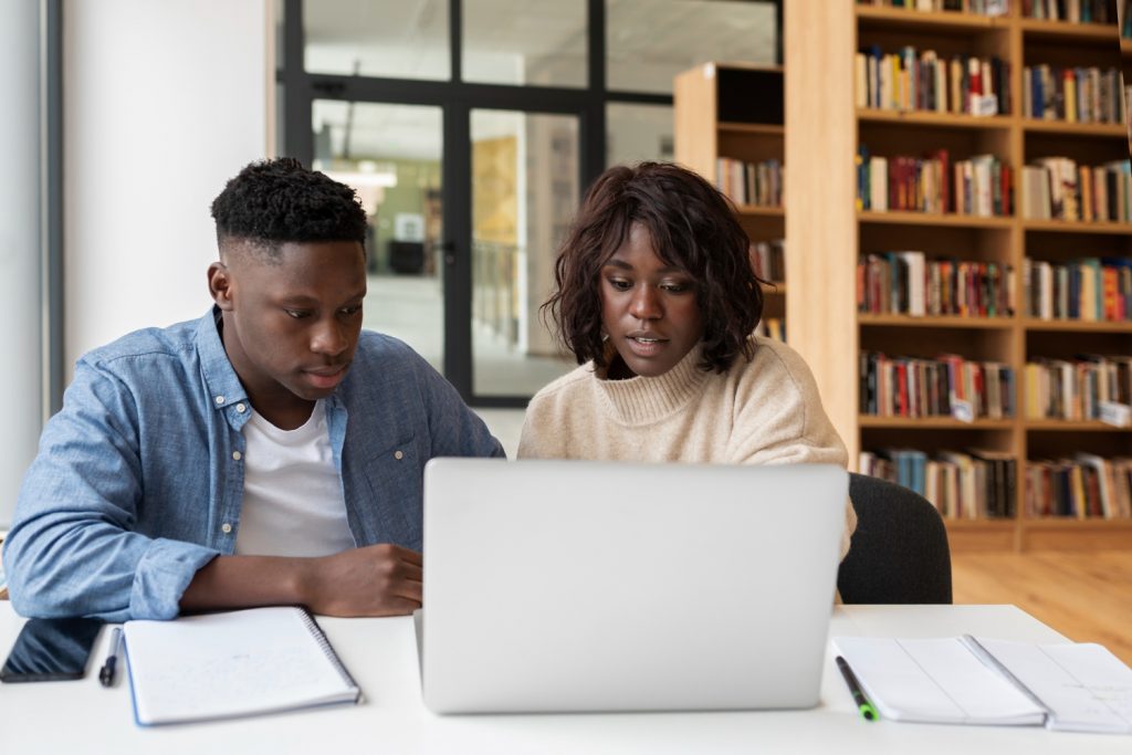 Black male and female student looking at laptop screen studying in the library