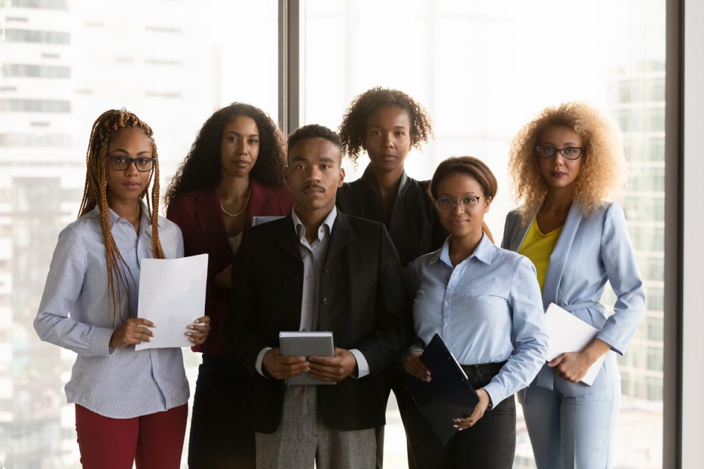 Group portrait of sincere young african american employees managers posing in modern workplace, successful motivated mixed race teammates in formal wear looking at camera, corporate career concept.